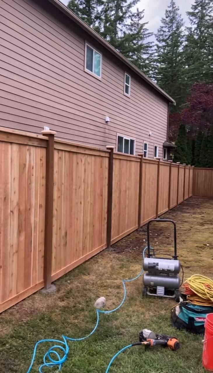 Long cedar privacy fence run with capped posts during installation