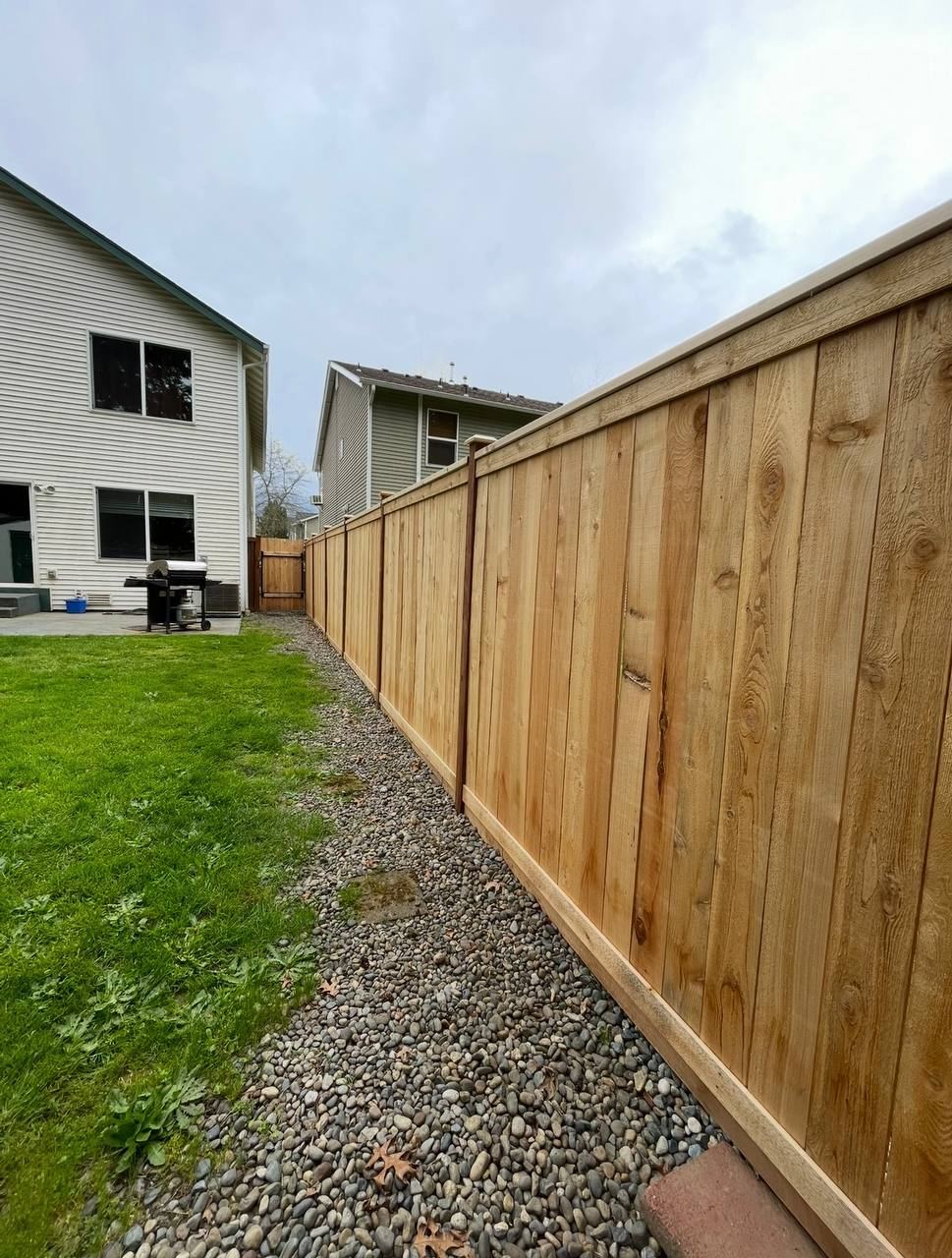 Cedar privacy fence with capped rails along river-rock border